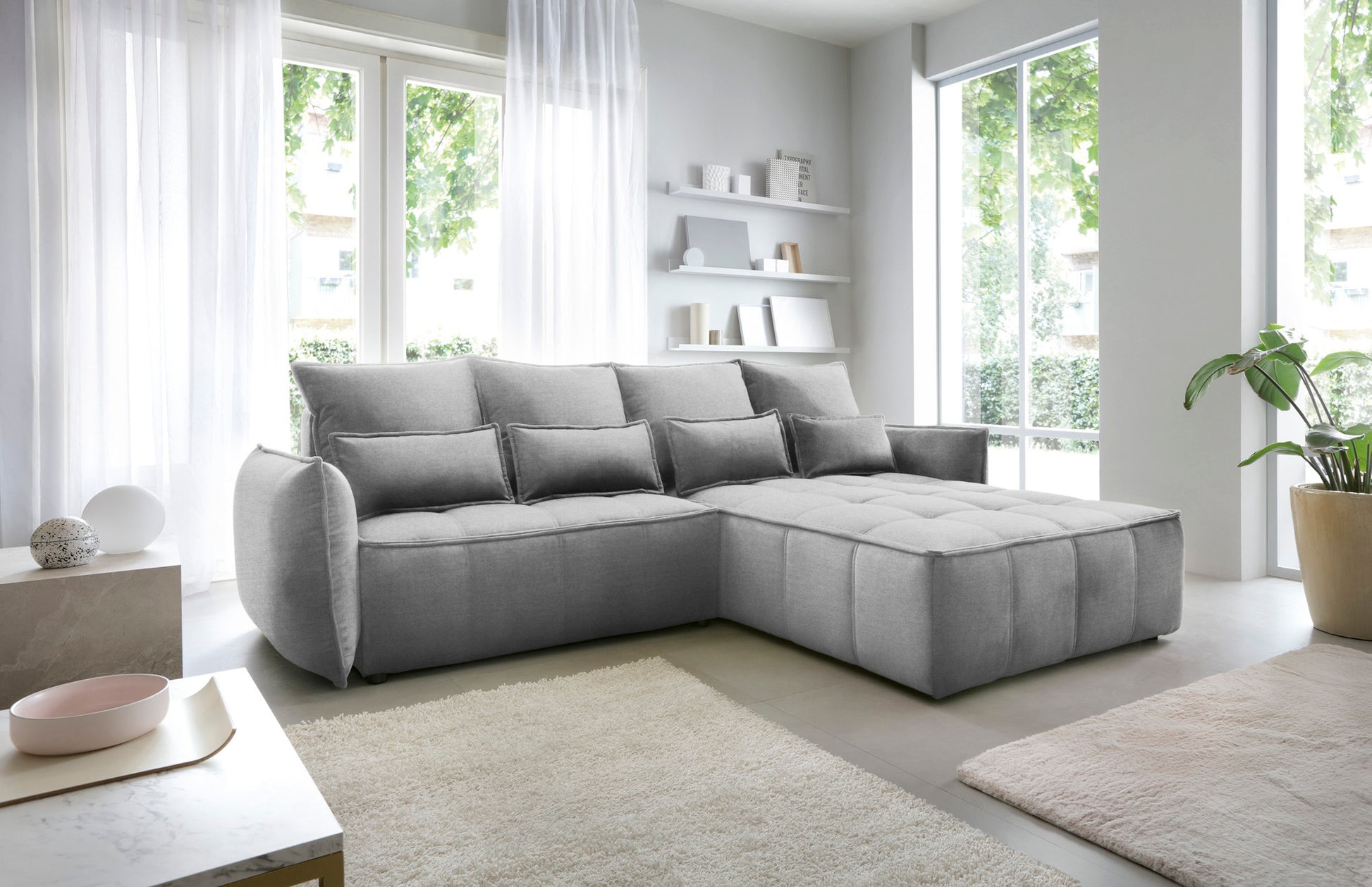 Narożnik Campo w układzie prawym, tapicerka Nube 04 szary, prezentowany w nowoczesnym wnętrzu z minimalistycznymi półkami i stolikiem kawowym.