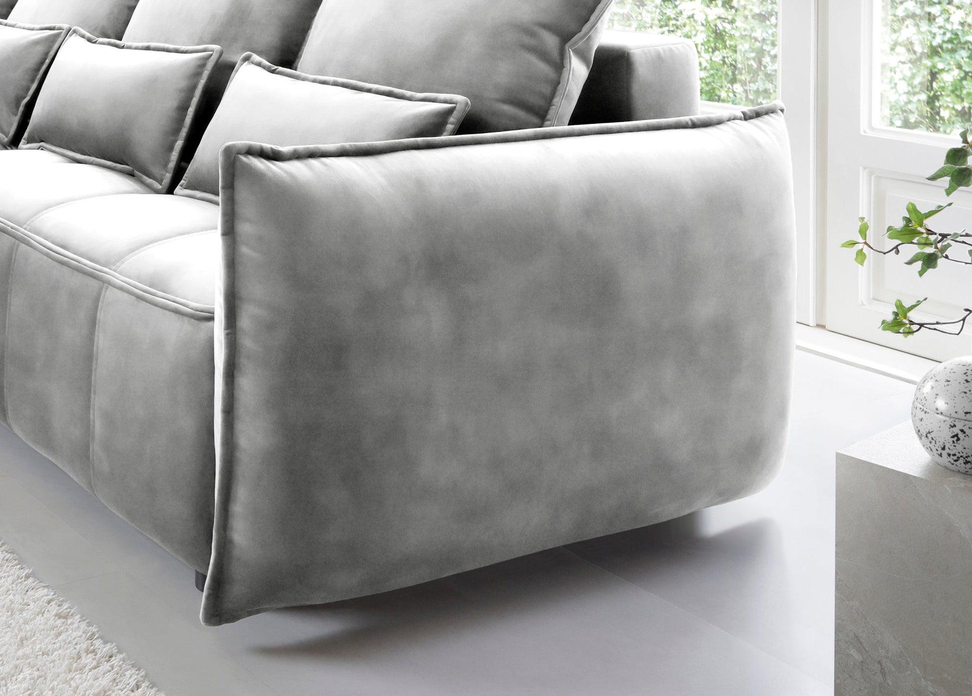 Detale tylnego podłokietnika narożnika Campo w układzie lewym, Relax 03 szary, z widoczną miękką obwódką i gładką tylną ścianką na tle okna.