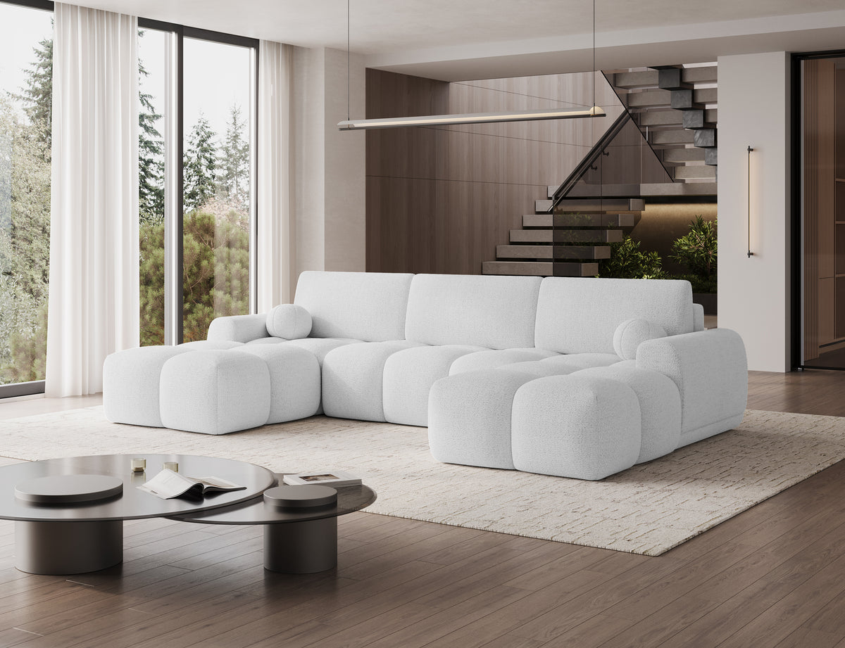 Narożnik Vianetto Royal 01 biały w nowoczesnym salonie z wysokimi oknami i schodami, widok z ukosa na dwie zaokrąglone otomany.
