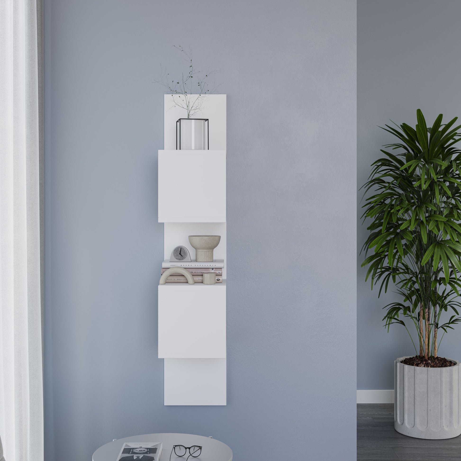 Biała półka Sunpedo zamontowana na jasnoniebieskiej ścianie, z doniczką na najwyższym segmencie i małym stolikiem kawowym z okularami i czasopismem.