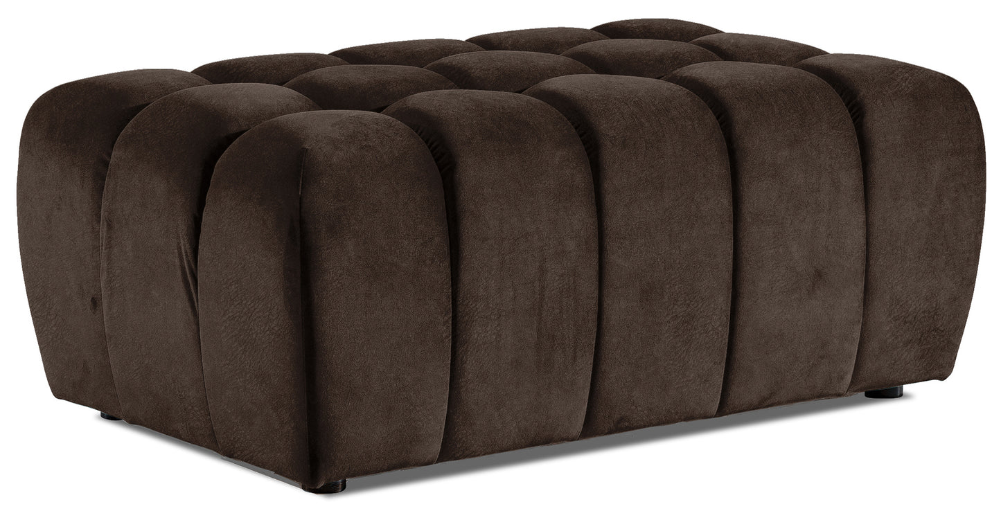 Pufa Lazaro w odcieniu Dora 28 brązowym, widoczna z przodu pod lekkim kątem, z charakterystycznymi, miękkimi przetłoczeniami i welurową tapicerką na jednolitym, białym tle.