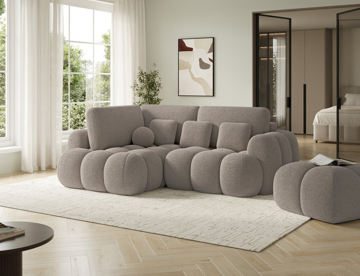 Pufa Covio w popielatej tkaninie Royal 20 w jasnej aranżacji salonu, ustawiona obok modułowego zestawu wypoczynkowego w salonie