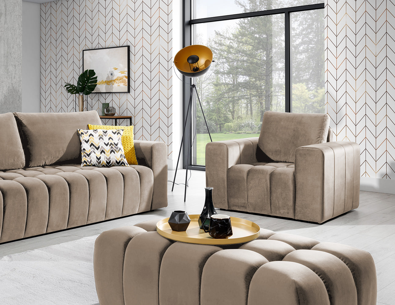 Pufa Lazaro Monolith 09 jasnobrązowa w aranżacji salonu: pufa ustawiona na środku wnętrza, przed sofą i fotelem w tym samym kolorze, na tle dekoracyjnej tapety w jodełkę, obok lampy na trójnogu i stolika kawowego z tacą.