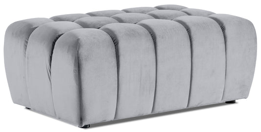 Pufa Lazaro Monolith 84 jasnoszara – widok perspektywiczny: prostokątna, pikowana pufa obita miękkim welwetem w chłodnym odcieniu szarości, z zaokrąglonymi pionowymi przetłoczeniami na całej powierzchni.