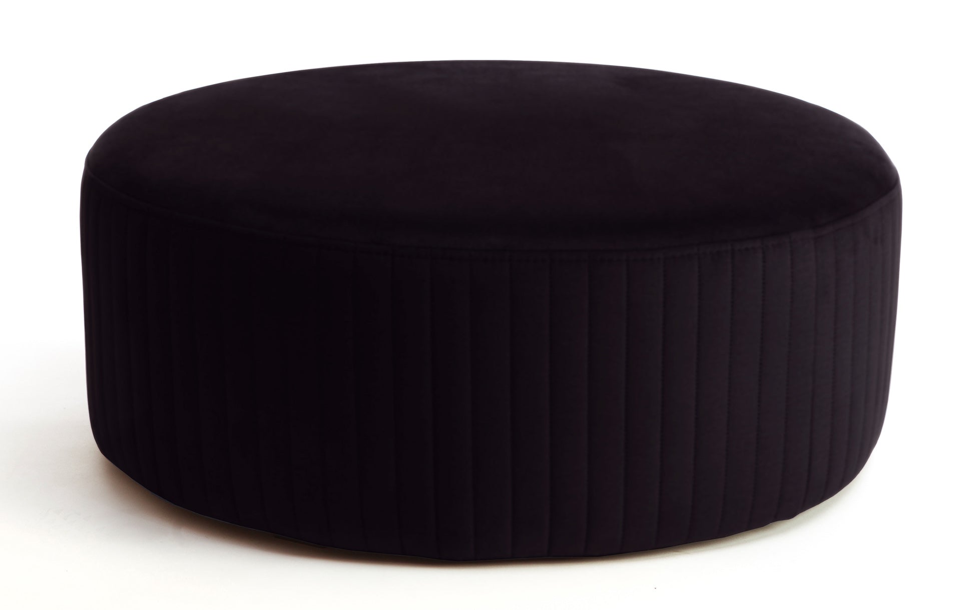 Pufa Lara w kolorze Mat Velvet 99 czarny, okrągła, tapicerowana welurem z pionowym przeszyciem po bokach, prezentowana na białym tle.