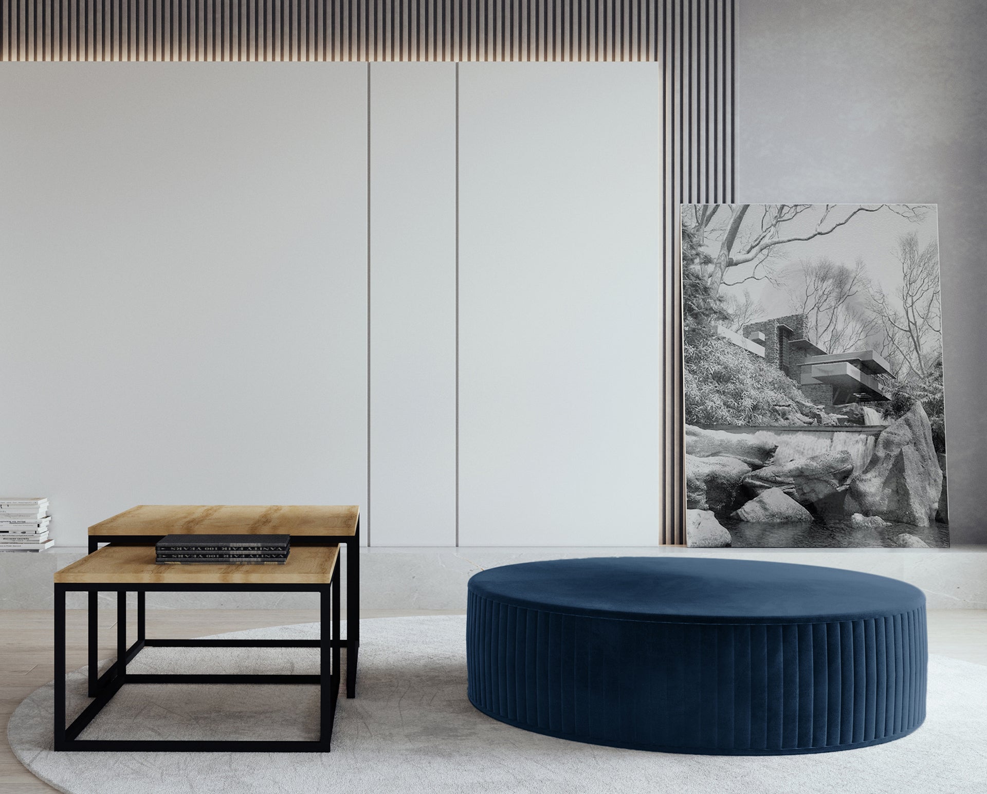 Pufa Lara w kolorze Monolith 77 niebieski, ustawiona w nowoczesnym salonie na jasnym dywanie, obok minimalistycznych stolików kawowych z drewnianym blatem i metalową podstawą