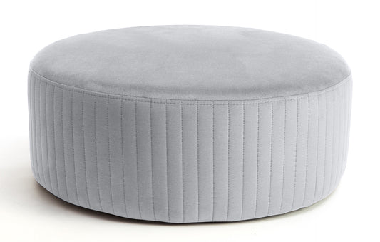 Pufa Lara w kolorze Monolith 84 jasnoszary, okrągła, tapicerowana welurem z pionowym przeszyciem po bokach, prezentowana na białym tle.