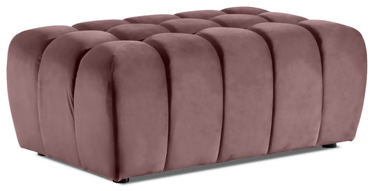 Prostokątna pufa Lazaro z charakterystycznymi, pionowymi, zaokrąglonymi przetłoczeniami, obita miękkim różowym welurem Matt Velvet 63, sfotografowana na białym tle.
