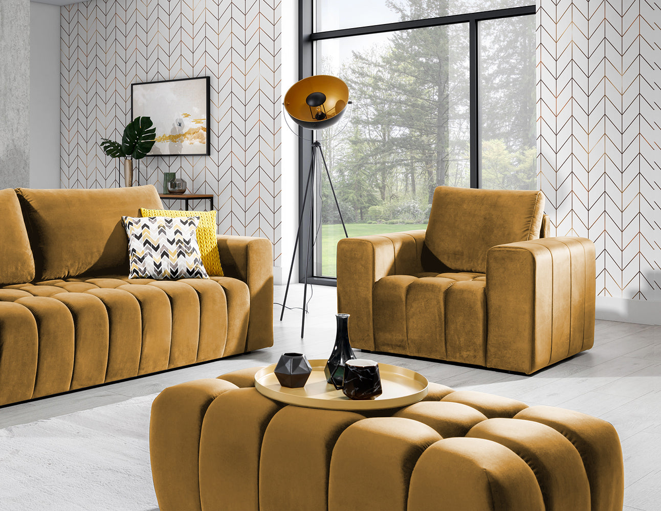Pufa Lazaro Monolith 48 żółta w aranżacji: pufa na pierwszym planie przed sofą i fotelem w tym samym kolorze, na tle geometrycznej tapety, obok lampy stojącej i stolika kawowego.
