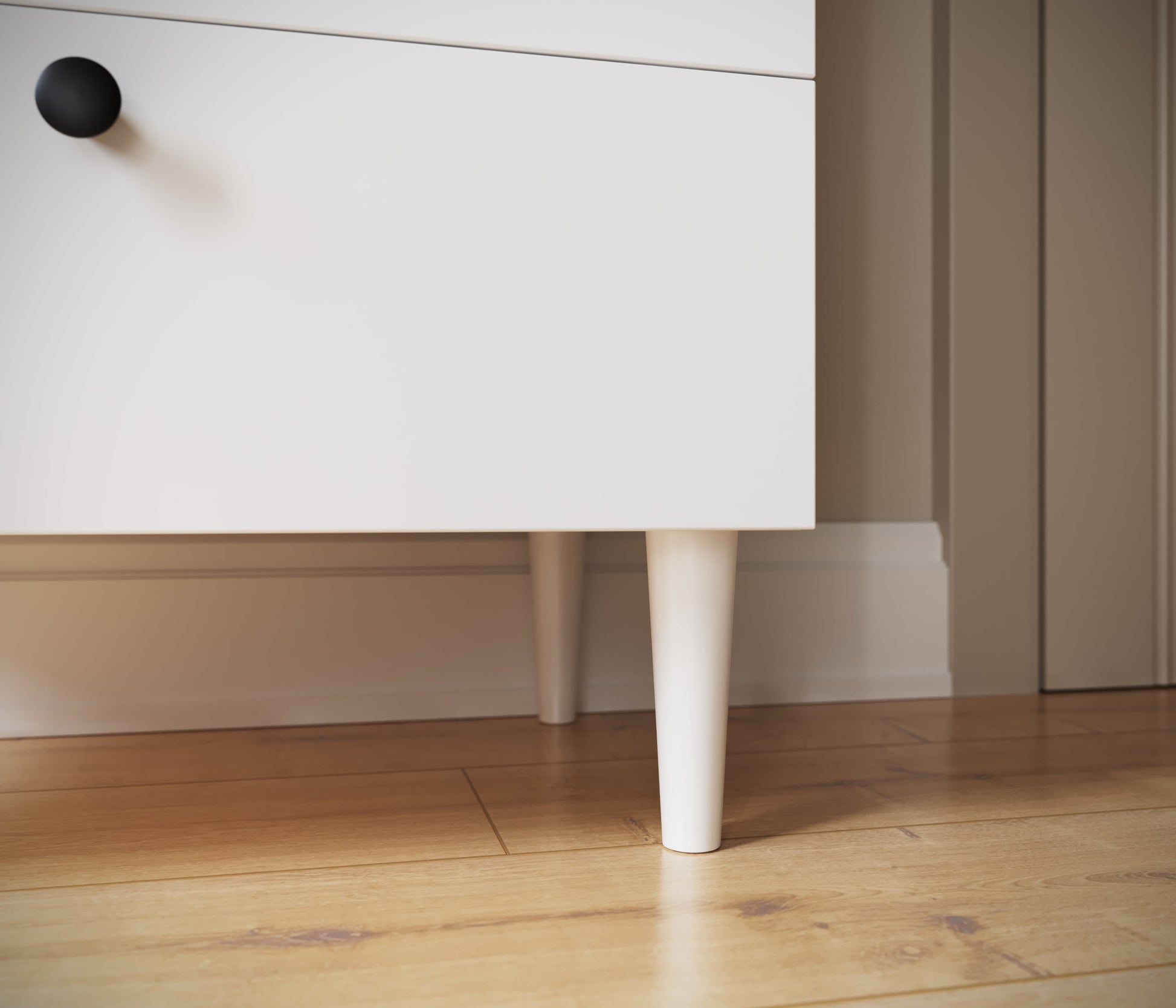 Biała noga regału Dullum – detal konstrukcyjny z widokiem na drewnianą podłogę.