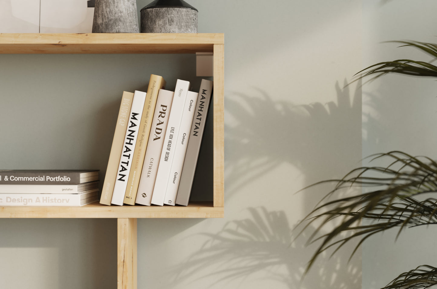 Zbliżenie na drewnianą półkę regału Egurro z książkami o designie i modzie, na tle jasnej ściany z cieniem liści palmowych.