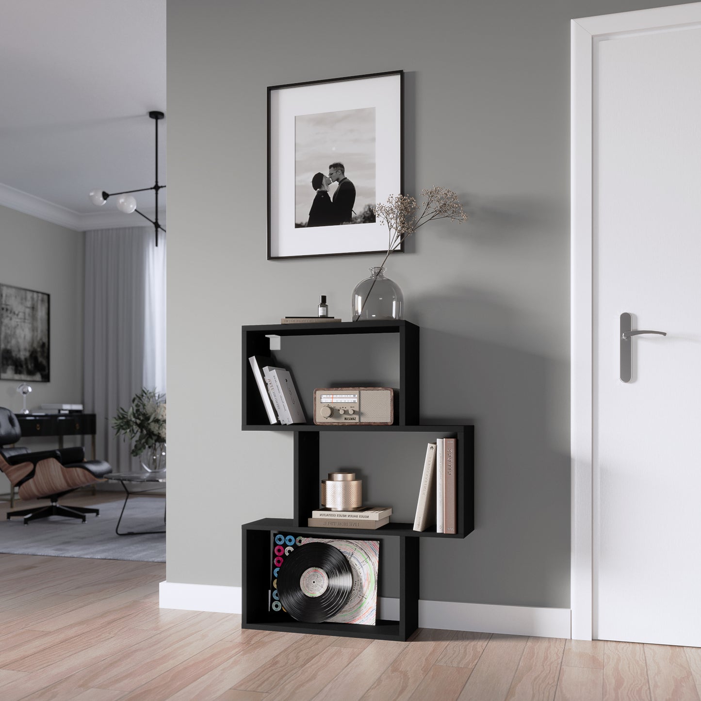 Czarny regał Evertti ustawiony przy szarej ścianie w salonie, wypełniony książkami, dekoracjami i winylami, obok białych drzwi.