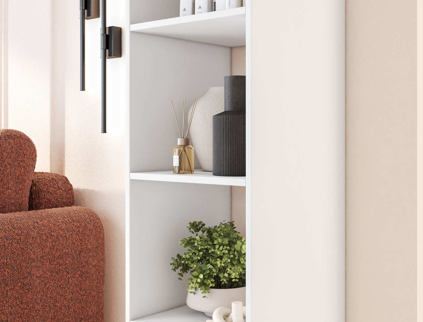 Fragment wnętrza z białym regałem Figgi, ozdobnym dyfuzorem, czarnym wazonem i rośliną, obok sofy w kolorze terakoty.