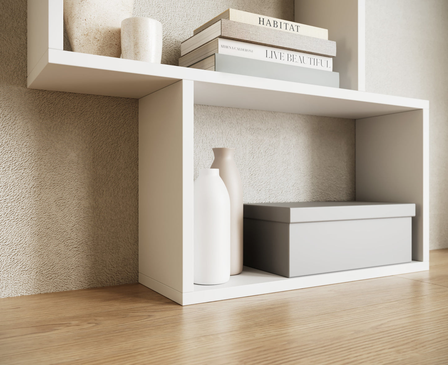 Dolna część białego regału Shellf z dekoracyjnymi wazonami, szarą pudełkową skrzynką i książkami na tle jasnej ściany. 