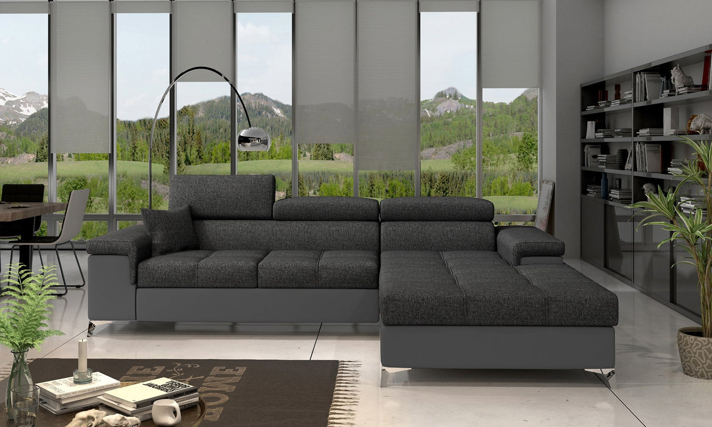 Narożnik Ricardo w kolorze Inari 96 ciemnoszary / Soft 29, układ prawy – aranżacja w salonie – nowoczesny narożnik w ciemnoszarej tkaninie z jasnymi elementami, ustawiony w przestronnym wnętrzu z dużym oknem.