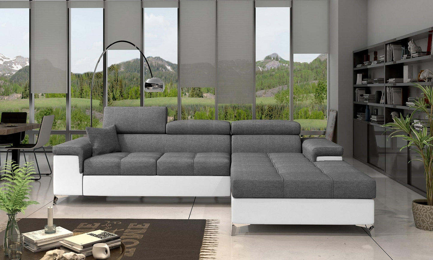 Narożnik Ricardo w kolorze Sawana 05 ciemnoszary / Soft 17, układ prawy – aranżacja w salonie – narożnik w ciemnoszarej tkaninie z jasnymi elementami, ustawiony w nowoczesnym wnętrzu z dużym oknem i minimalistycznym wystrojem.