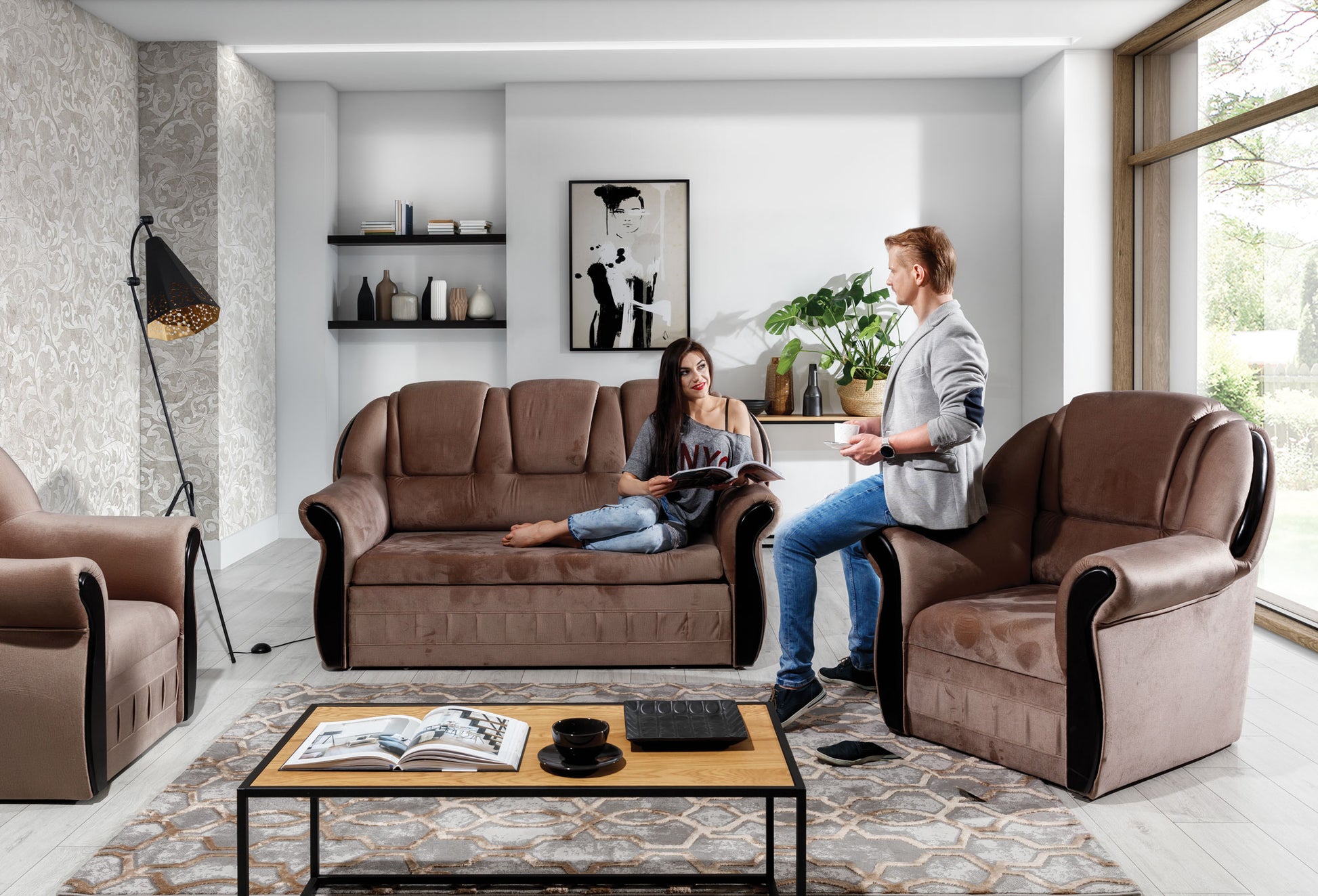 Sofa dwuosobowa i fotel Lord Monolith 09 w kolorze cappuccino ustawione przy stolikach kawowych na wzorzystym dywanie. Wyraźna faktura materiału i masywne podłokietniki tworzą solidny wizualnie zestaw.