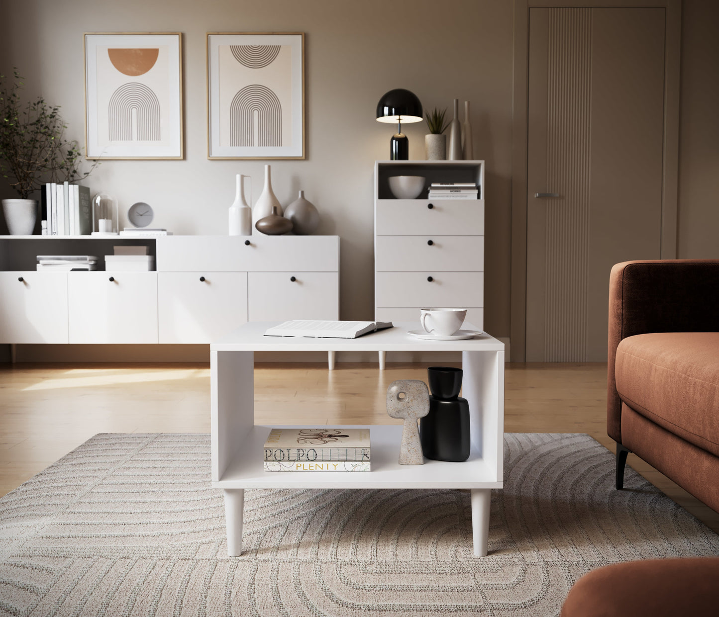 Biały stolik kawowy Dullum w nowoczesnym salonie – ustawiony na wzorzystym dywanie, z książką, filiżanką i dekoracją, w tle meble z tej samej kolekcji.