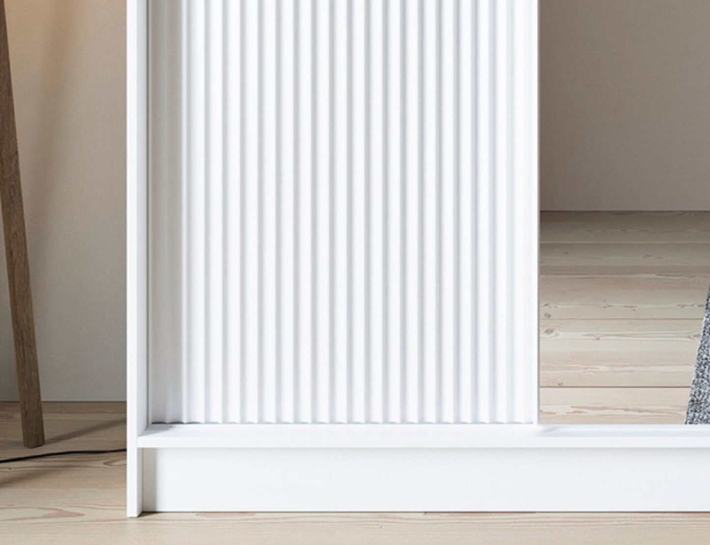 Zbliżenie na dolny fragment drzwi ryflowanych w białej szafie Biancco III z lustrem, eleganckie i minimalistyczne wykończenie.