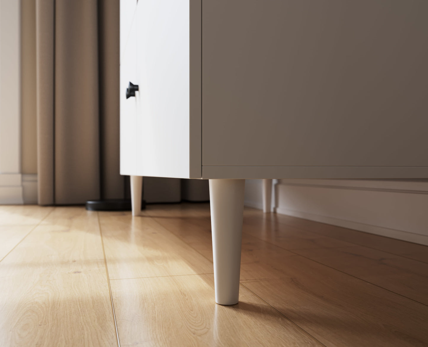 Biała noga szafy Dullum ustawionej na drewnianej podłodze – solidna i stabilna podstawa mebla.