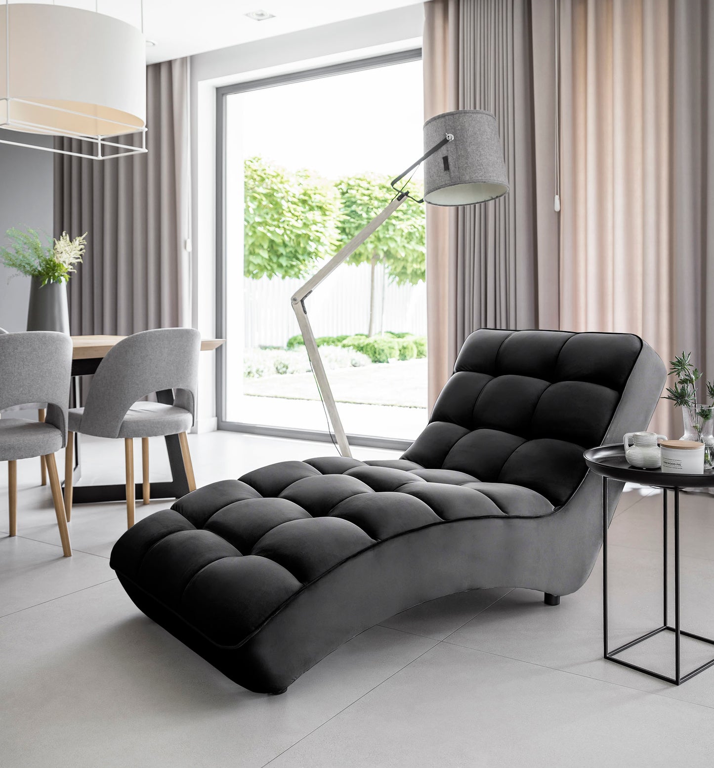 Szezlong Loren Loco 10 czarny ustawiony w jasnym salonie z dużym oknem, obok stolika i lampy podłogowej.