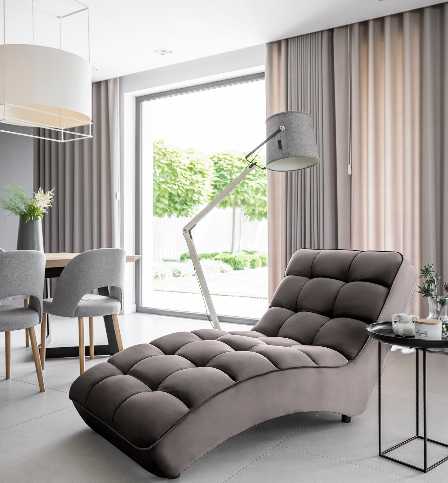 Ciemnoszary szezlong Loren w eleganckim salonie, w towarzystwie zasłon, dużego okna i minimalistycznej lampy podłogowej.