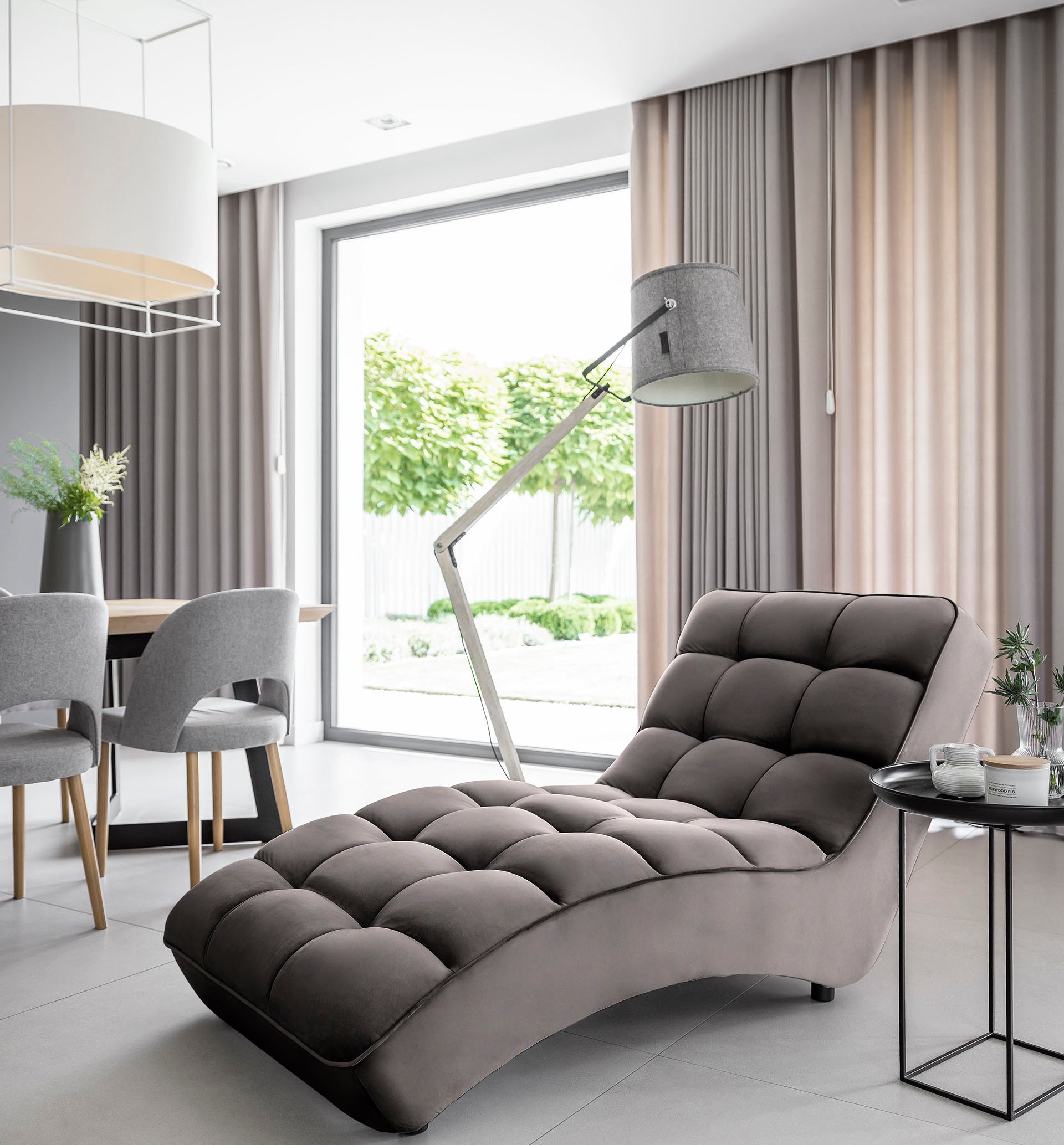 Ciemnoszary szezlong Loren w eleganckim salonie, w towarzystwie zasłon, dużego okna i minimalistycznej lampy podłogowej.