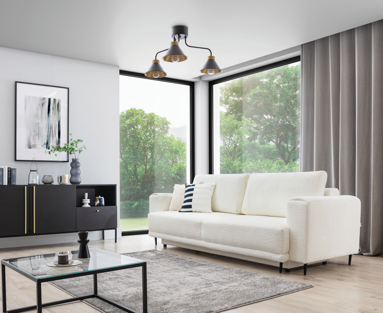 Nowoczesny, jasny salon z dużym oknem, w którym nad czarną komodą i białym fotelem zwisa lampa sufitowa Detmer 3 z trzema metalowymi kloszami.