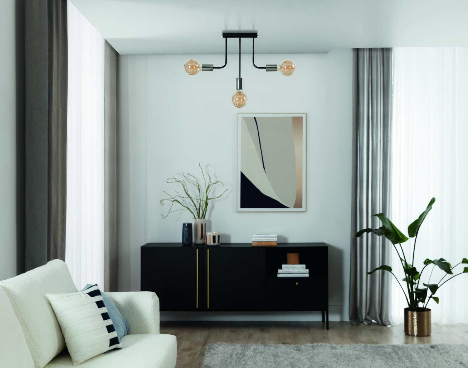 Żyrandol Indigeo 48x48 cm z trzema źródłami światła w nowoczesnym salonie z jasnymi zasłonami i czarną komodą.