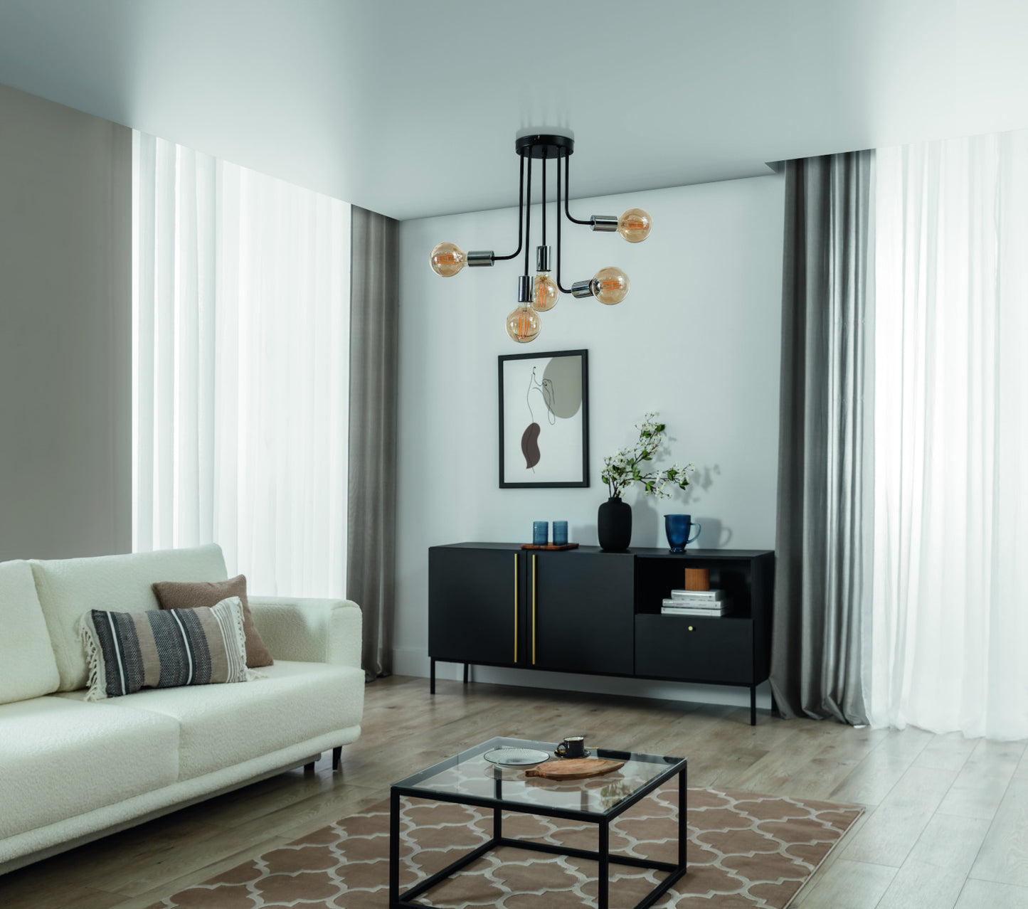 Żyrandol Indigeo I 47x55 cm z pięcioma dekoracyjnymi żarówkami w nowoczesnym salonie z dużymi oknami i minimalistycznym wystrojem.