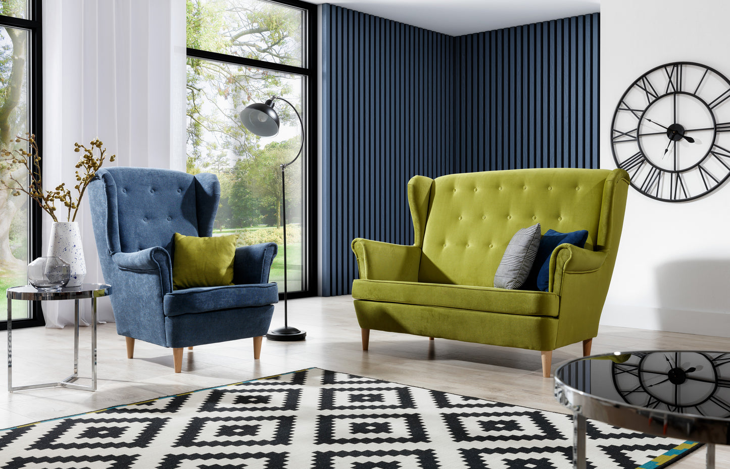 Komplet wypoczynkowy Aros w tkaninach Omega 86 zielony i Kronos 17 niebieski – elegancki fotel i sofa w nowoczesnym salonie z dużymi oknami i geometrycznym dywanem.
