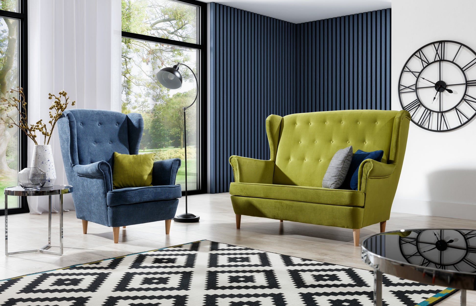 Komplet wypoczynkowy Aros w tkaninach Omega 86 zielony i Kronos 17 niebieski – elegancki fotel i sofa w nowoczesnym salonie z dużymi oknami i geometrycznym dywanem.